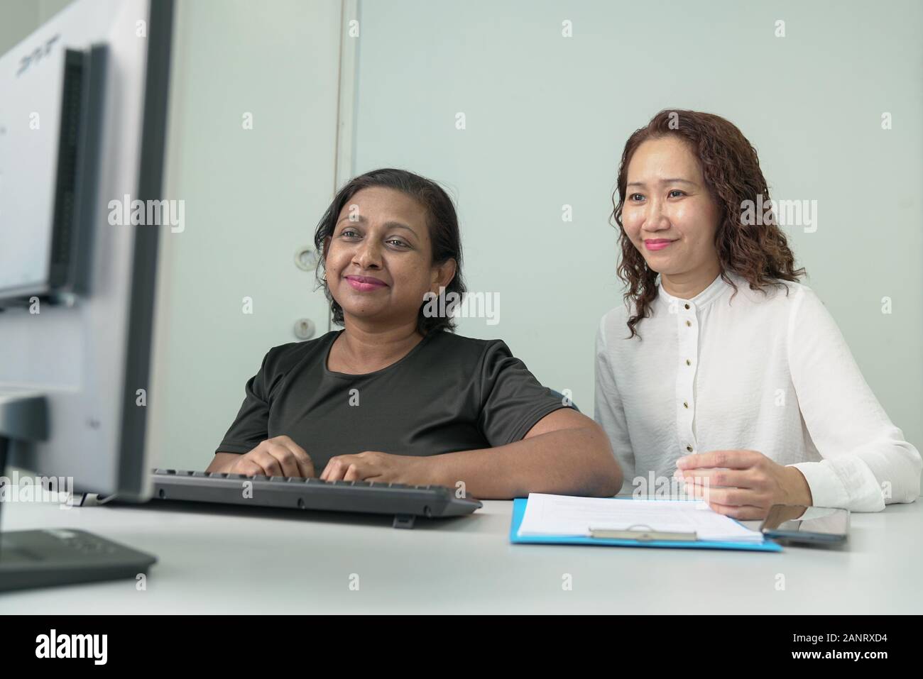 Two businesswomen or corporate professionals working together and in a discussion. Office table with computer. Stock Photo