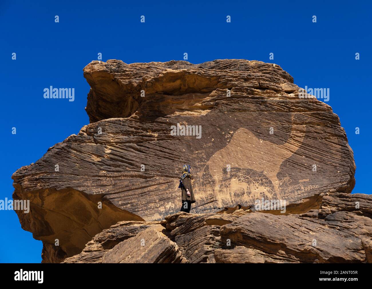 Tourist standing in front of a life-sized camel petroglyph on a rock, Najran Province, Thar, Saudi Arabia Stock Photo
