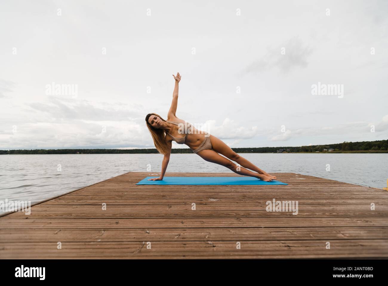 Fit Slim Woman Practicing Yoga Exercises Wearing Mini Swimsuit Bikini At Lake With Clouds Yoga