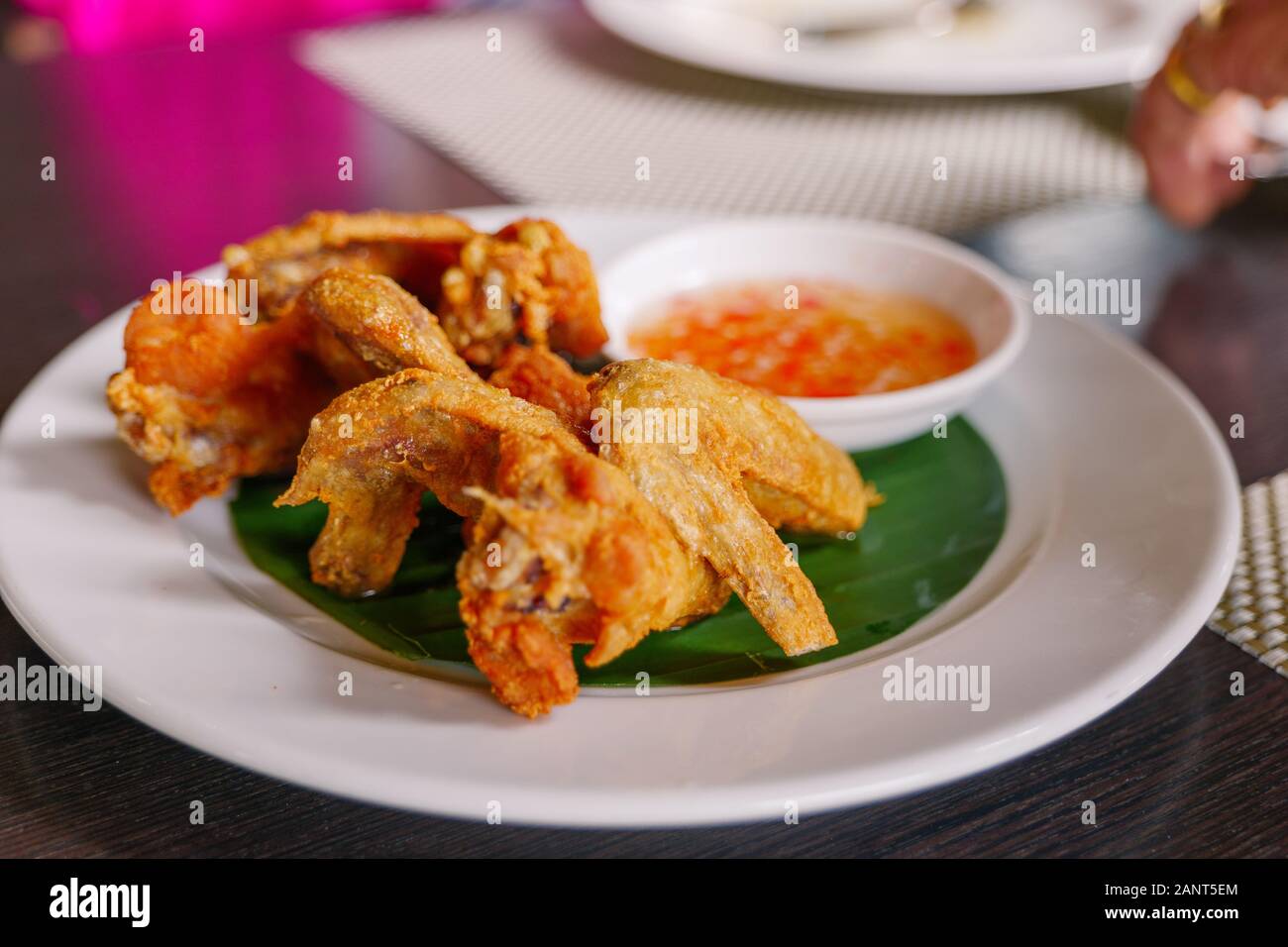 Thai style deep fried crispy chicken wing, serve on white dish with spicy sweet sauce on side. Thai famous appetizer dish. Stock Photo