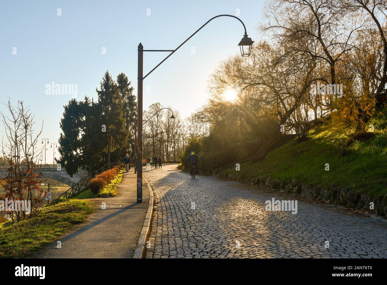 Backlight view of river sidewalk Lungo Po Armando Diaz with people walking and cycling in a sunny winter day, Turin, Piedmont, Italy Stock Photo
