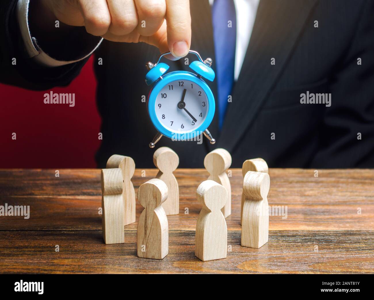 A businessman holds a blue clock over a team of workers. Time management concept. Deadline. Teamwork. Scrum. Human resources. Business meeting. Planni Stock Photo