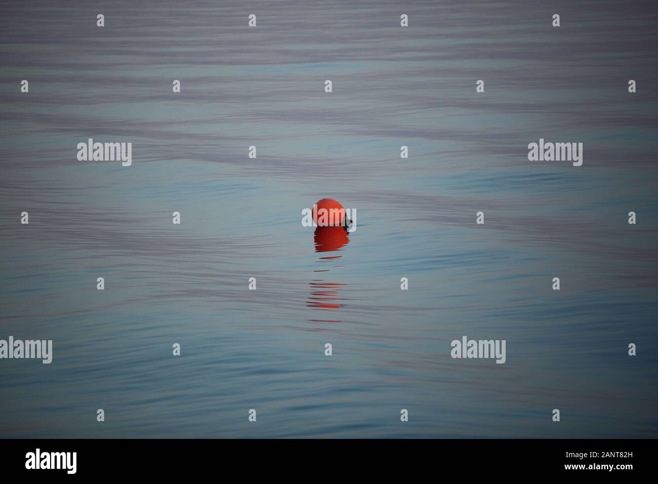 Red buoy in middle of sea / ocean / lake, reflections in water, nobody, oneiric calm silent atmosphere. Stock Photo