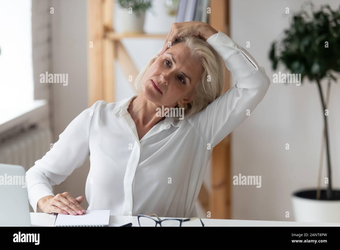 Middle-aged businesswoman seated at office workplace do gymnastics Stock Photo