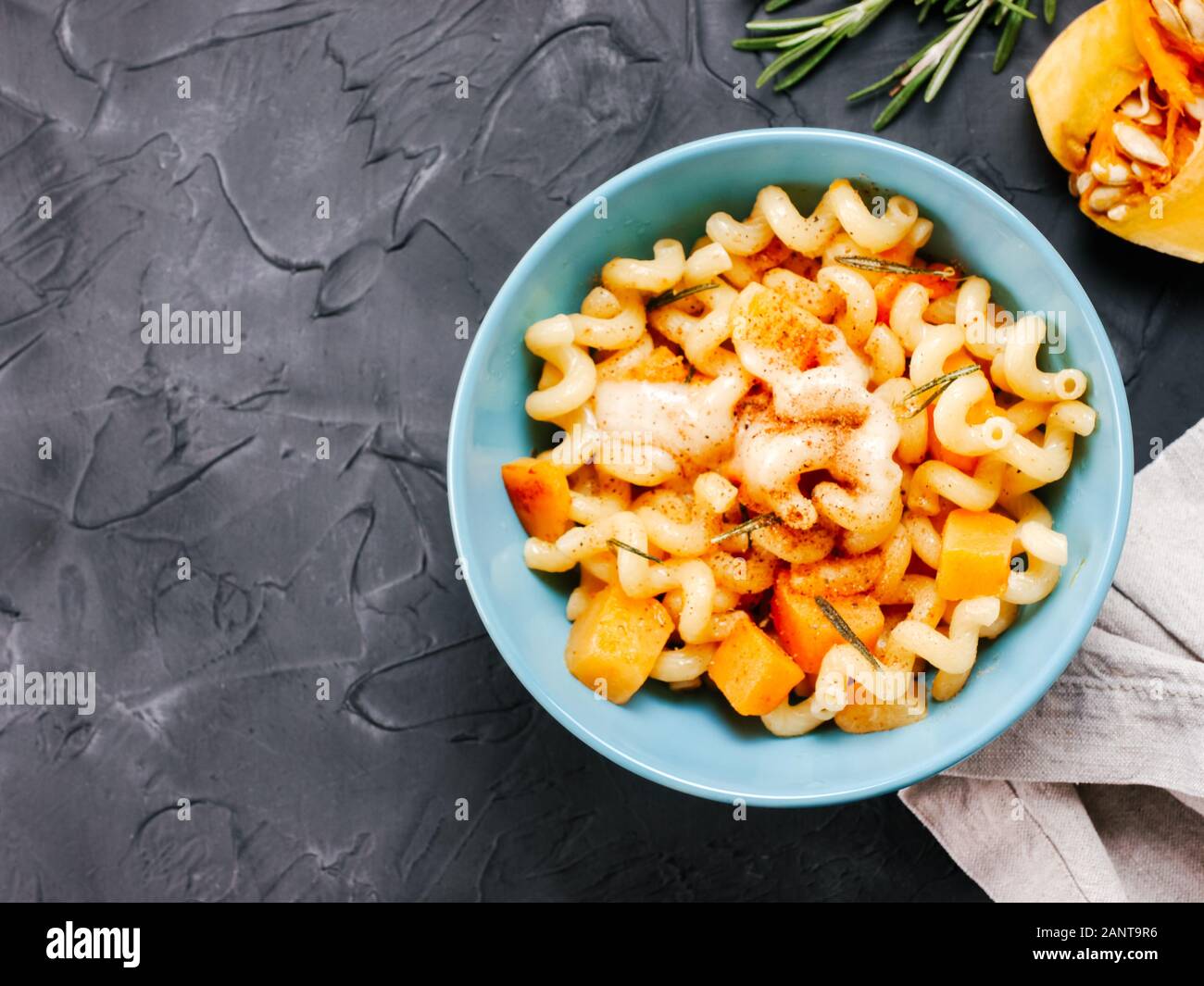 Fusilli pasta with pumpkin, rosemary and brie cheese. Idea recipe pasta. Vegetarian food. Homemade pasta dish in blue bowl over black concrete background. Copy space. Top view or flat lay. Stock Photo