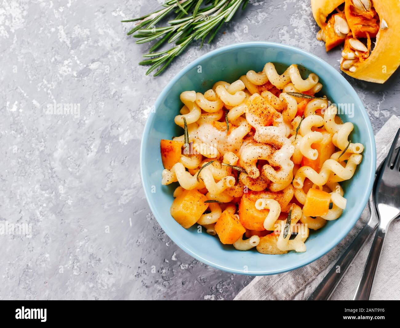 Fusilli pasta with pumpkin, rosemary and brie cheese. Idea recipe pasta. Vegetarian food. Homemade pasta dish in blue bowl over gray concrete background. Copy space. Top view or flat lay. Stock Photo