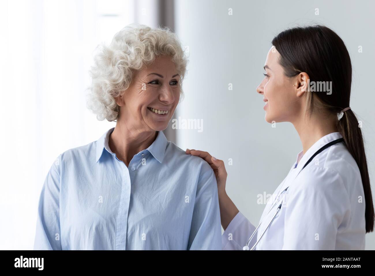 Caring nurse touching smiling older woman shoulder, expressing support Stock Photo