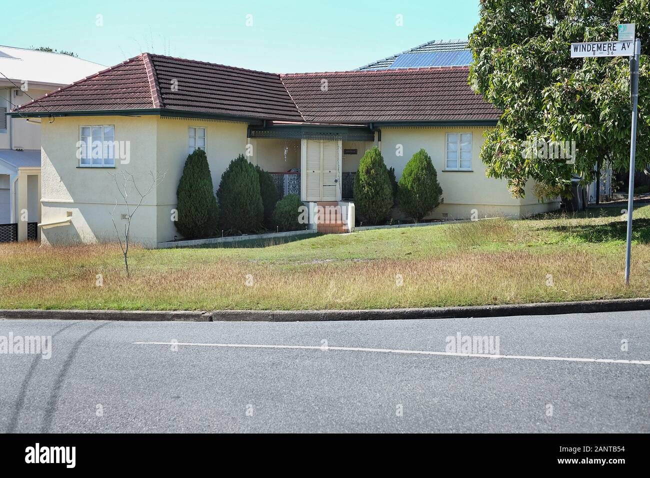 An original, L shape, post war house on a grassy corner block with small conifer trees flanking the front door, in the Brisbane suburb of Cannon Hill Stock Photo