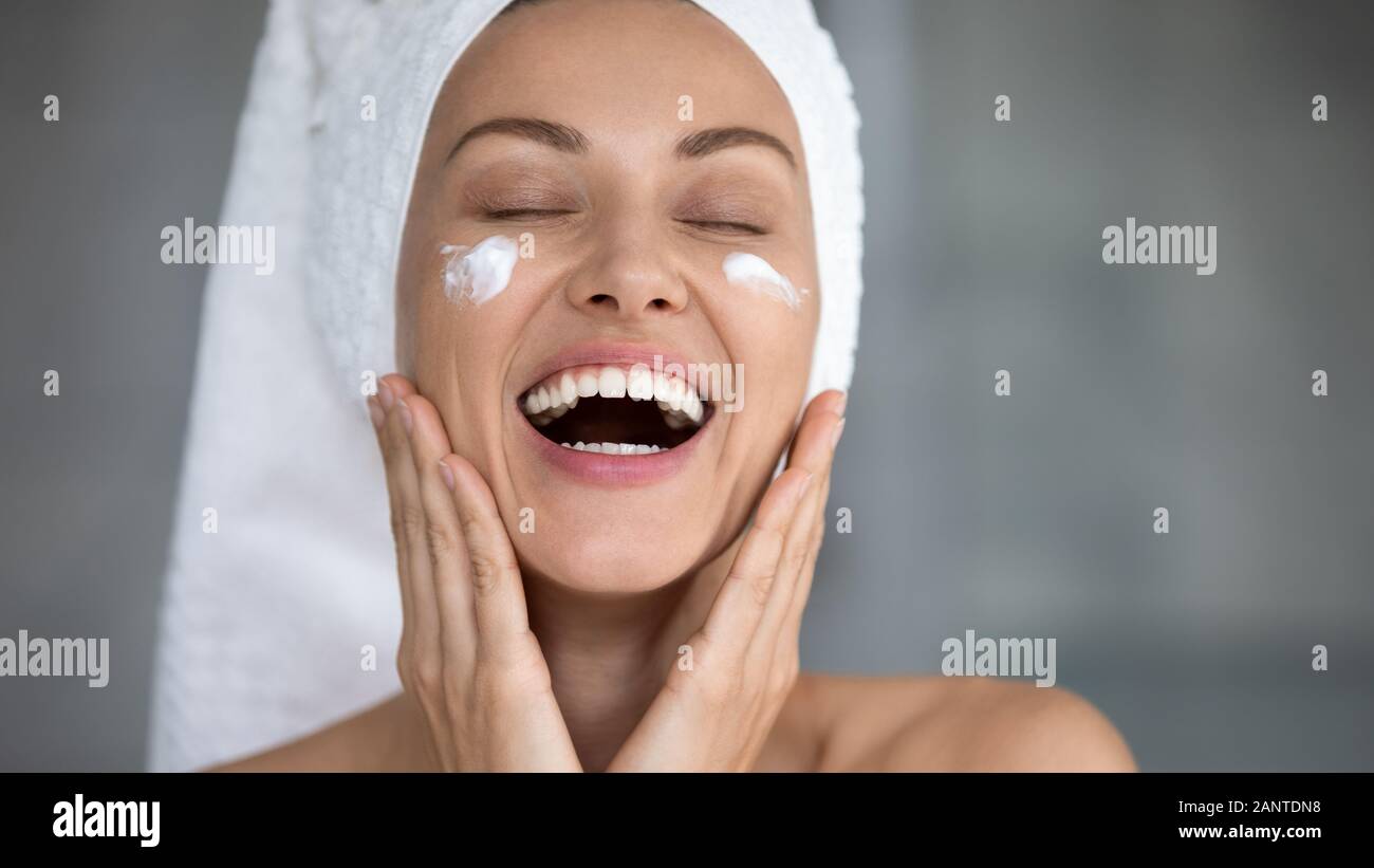 Close up excited beautiful woman laughing, applying moisturizing cream Stock Photo