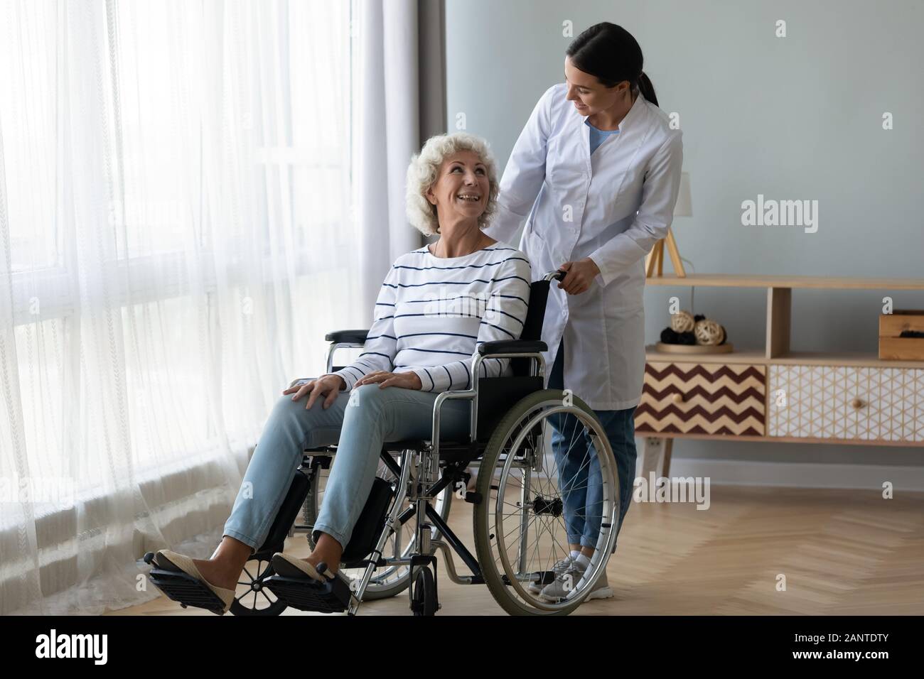 Caregiver helping disabled older woman in wheelchair at home Stock Photo