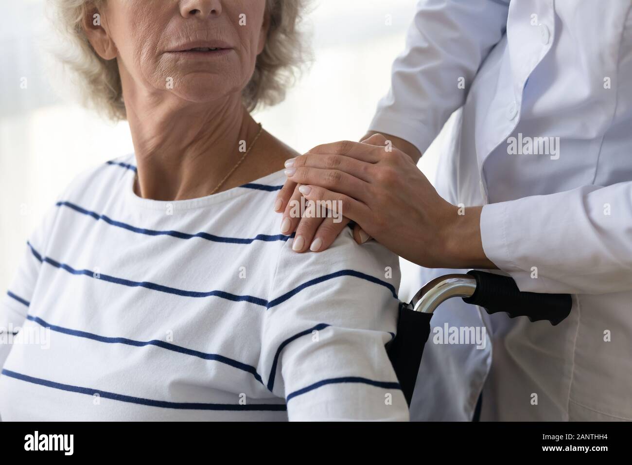 Caregiver supporting disabled older woman, holding hands on shoulder Stock Photo