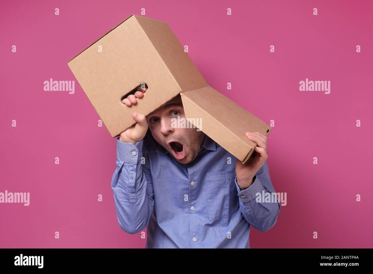 Man in blue shirt with a brown paper box on his head, hiding from job stress. Studio shot Stock Photo