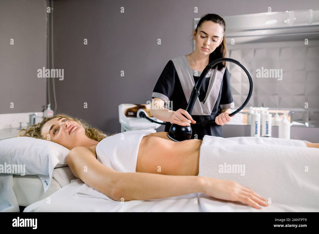 Attractive young blond woman client with slim fit body getting anticellulite and anti fat therapy in beauty salon on her belly. Skin and body care Stock Photo