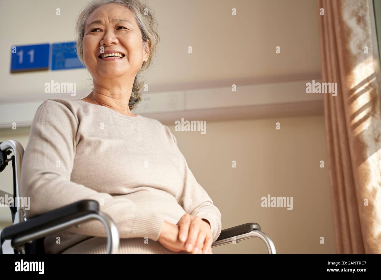 happy senior asian woman sitting in wheel chair in her room in nursing home, happy and smiling Stock Photo