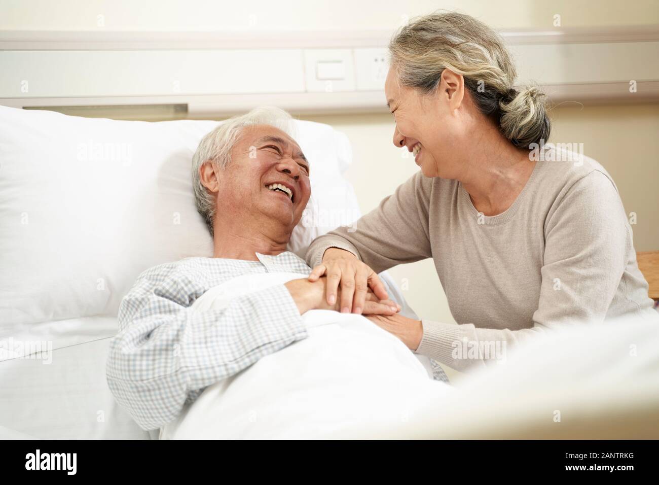 loving and caring senior asian woman visiting and talking to hospitalized husband at bedside Stock Photo