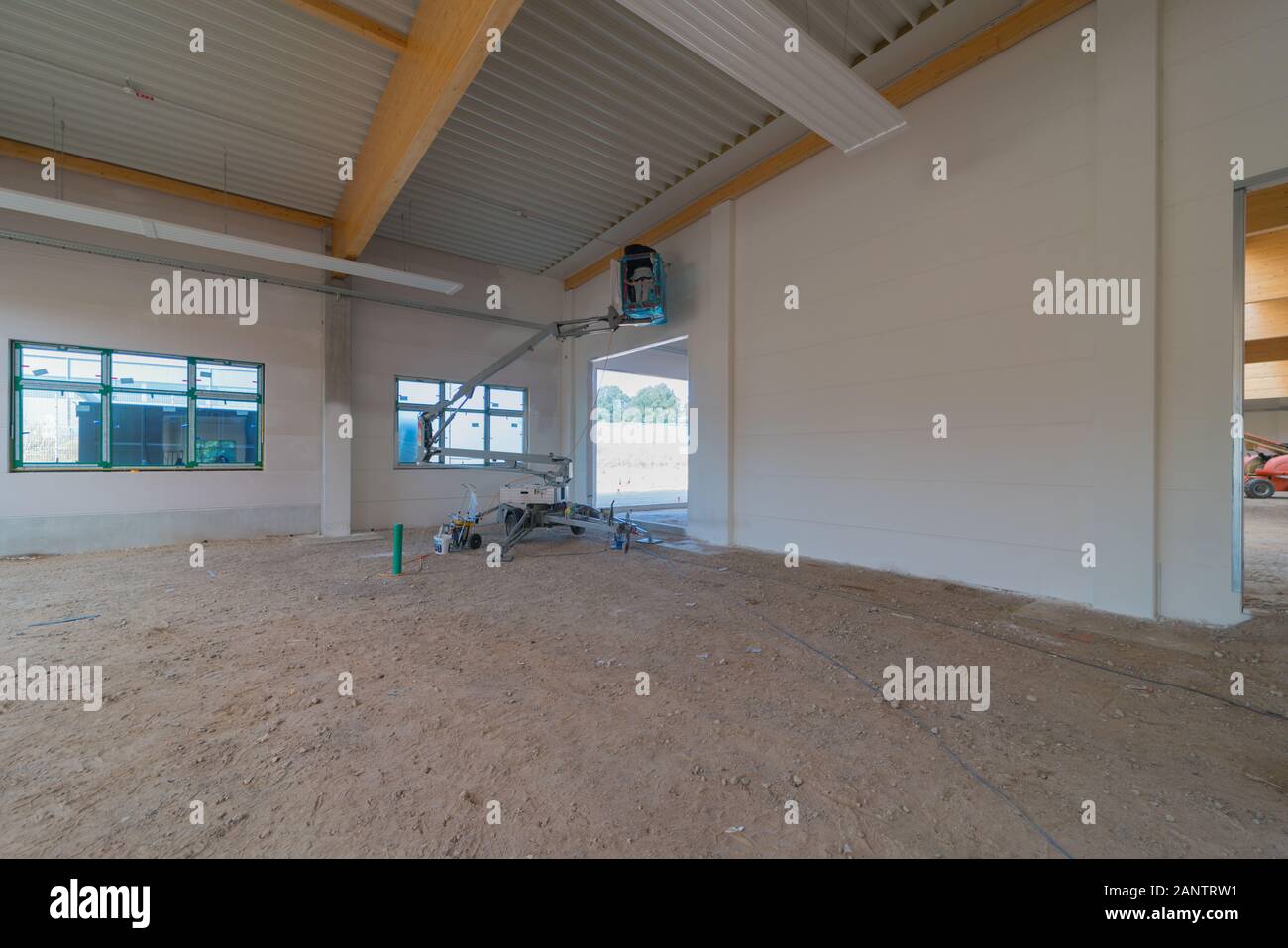 Inside a large factory building, the walls are sprayed white by a painter on a telescopic machine Stock Photo