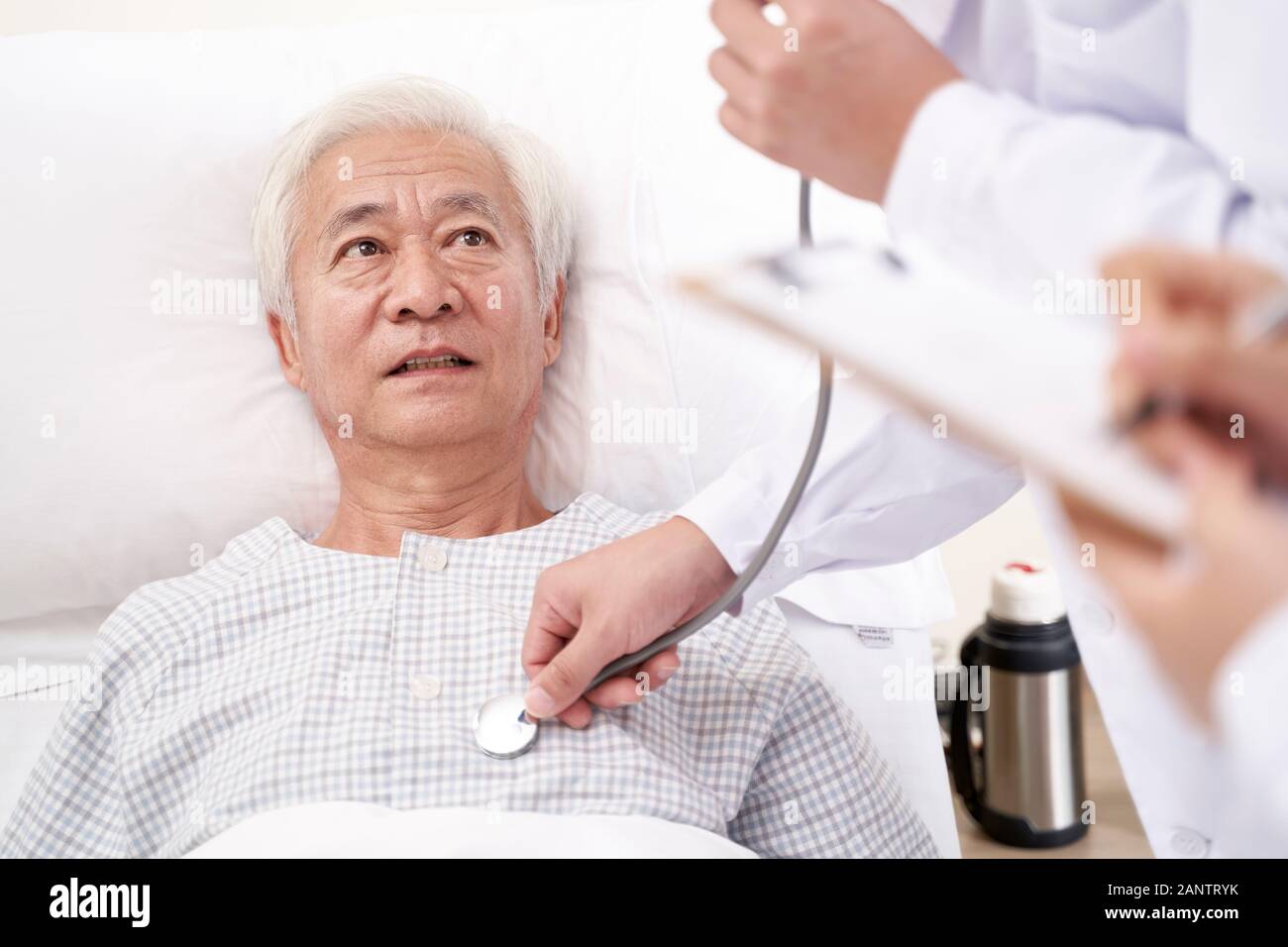 asian old man lying in bed in hospital ward being examined by doctor