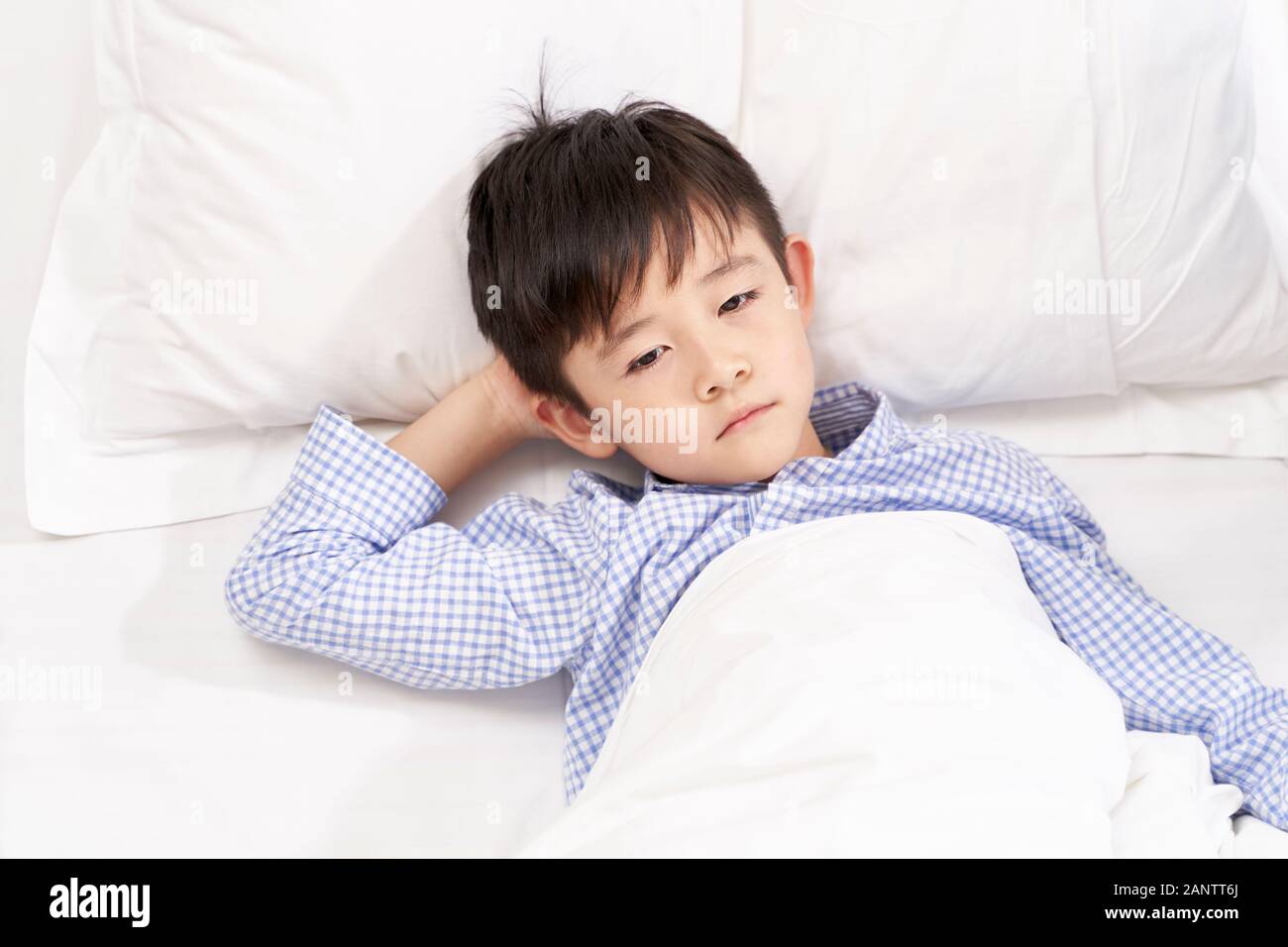 five year old child lying in bed in hospital ward looking sad and depressed Stock Photo