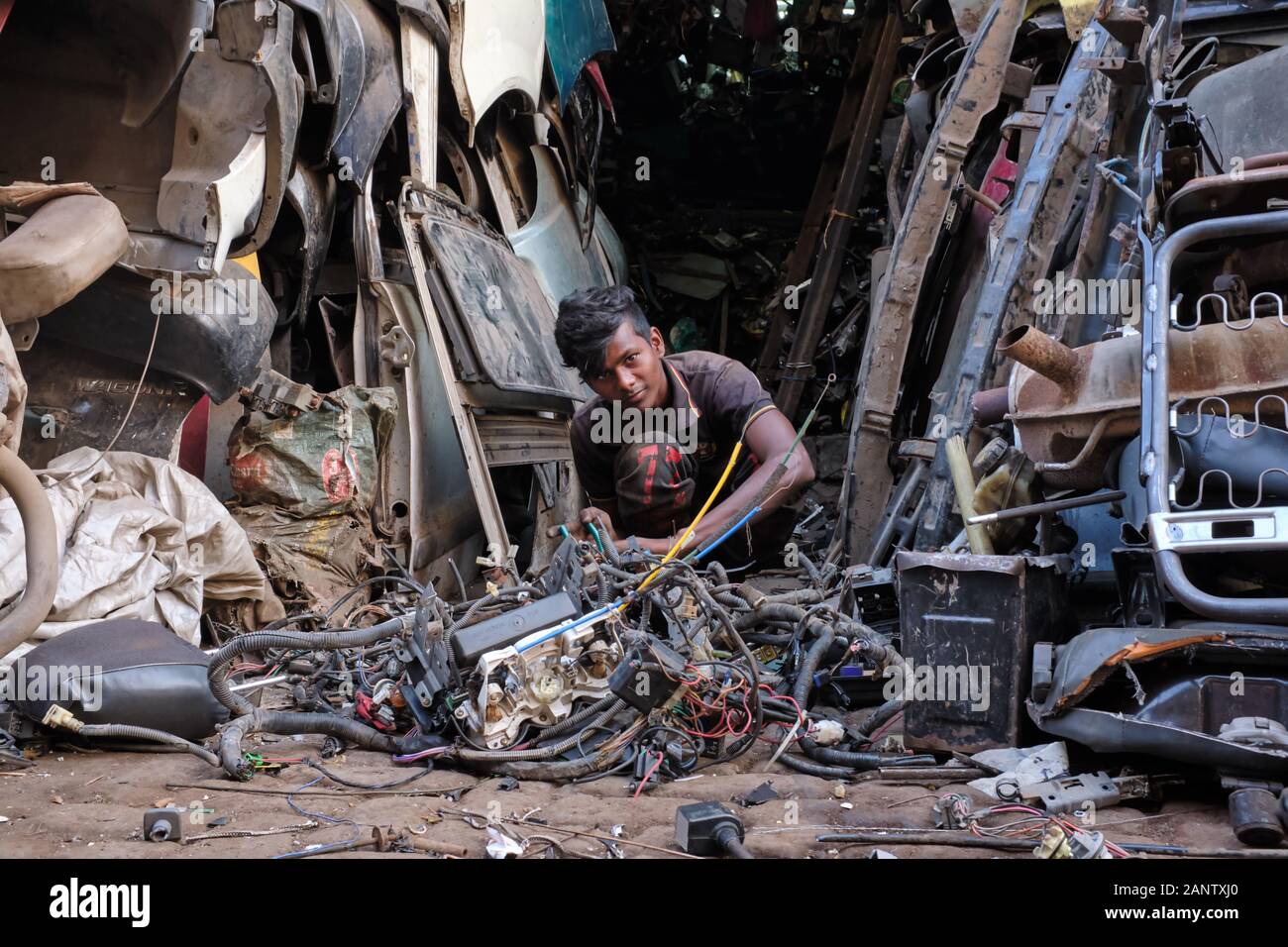 A worker taking apart parts of dismantled old cars at Thieves' Market (Chor Bazar) in Mumbai, India, surrounded by a mountain of old car parts Stock Photo