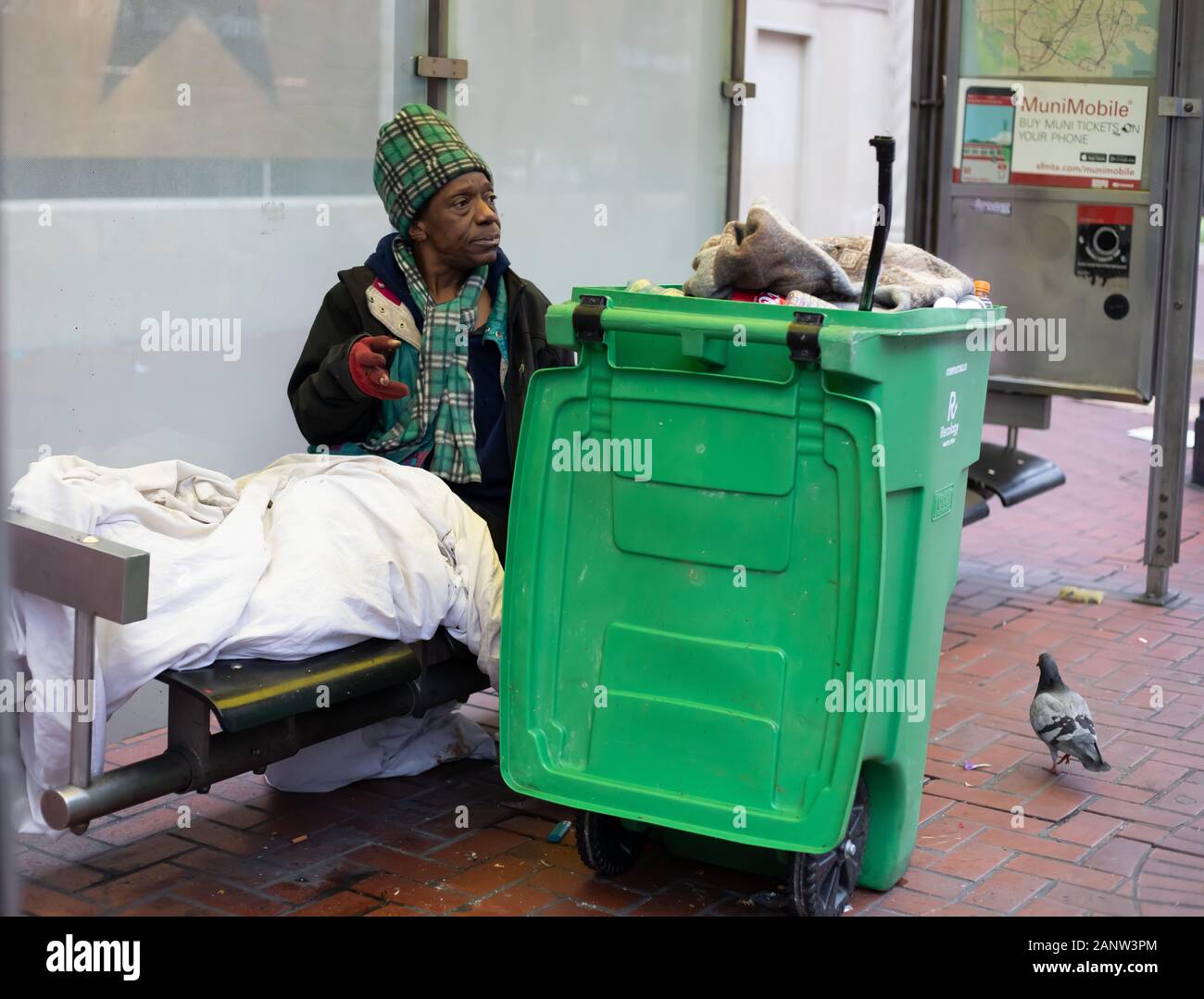 A homeless person makes a bus stop seat his temporary bed, with his