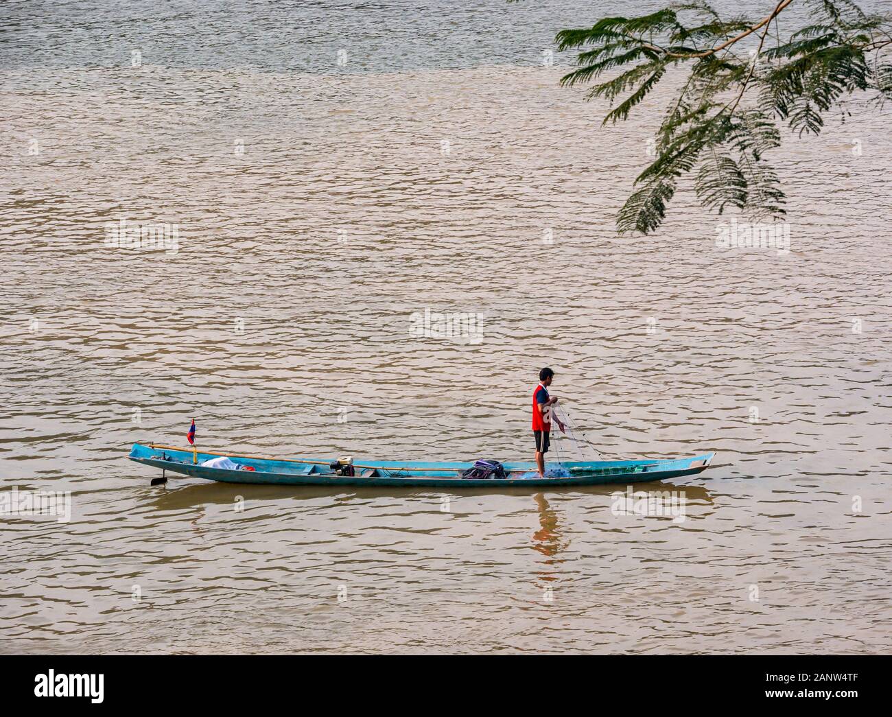 Local man fishing from traditional dugout canoe, Mekong River, Luang Prabang, Laos Stock Photo