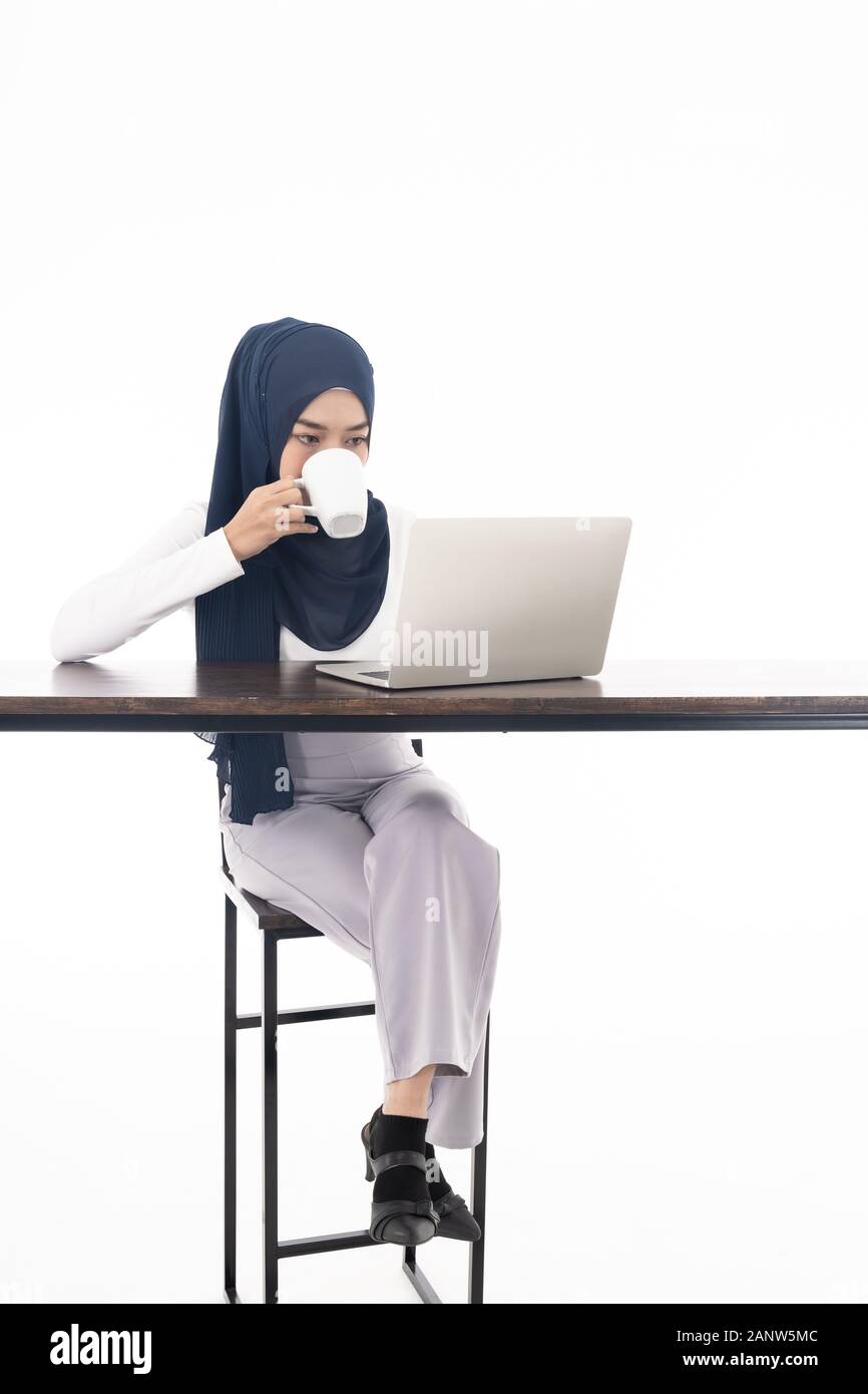 Asian young adult woman wearing hijab using laptop and sipping coffee ...