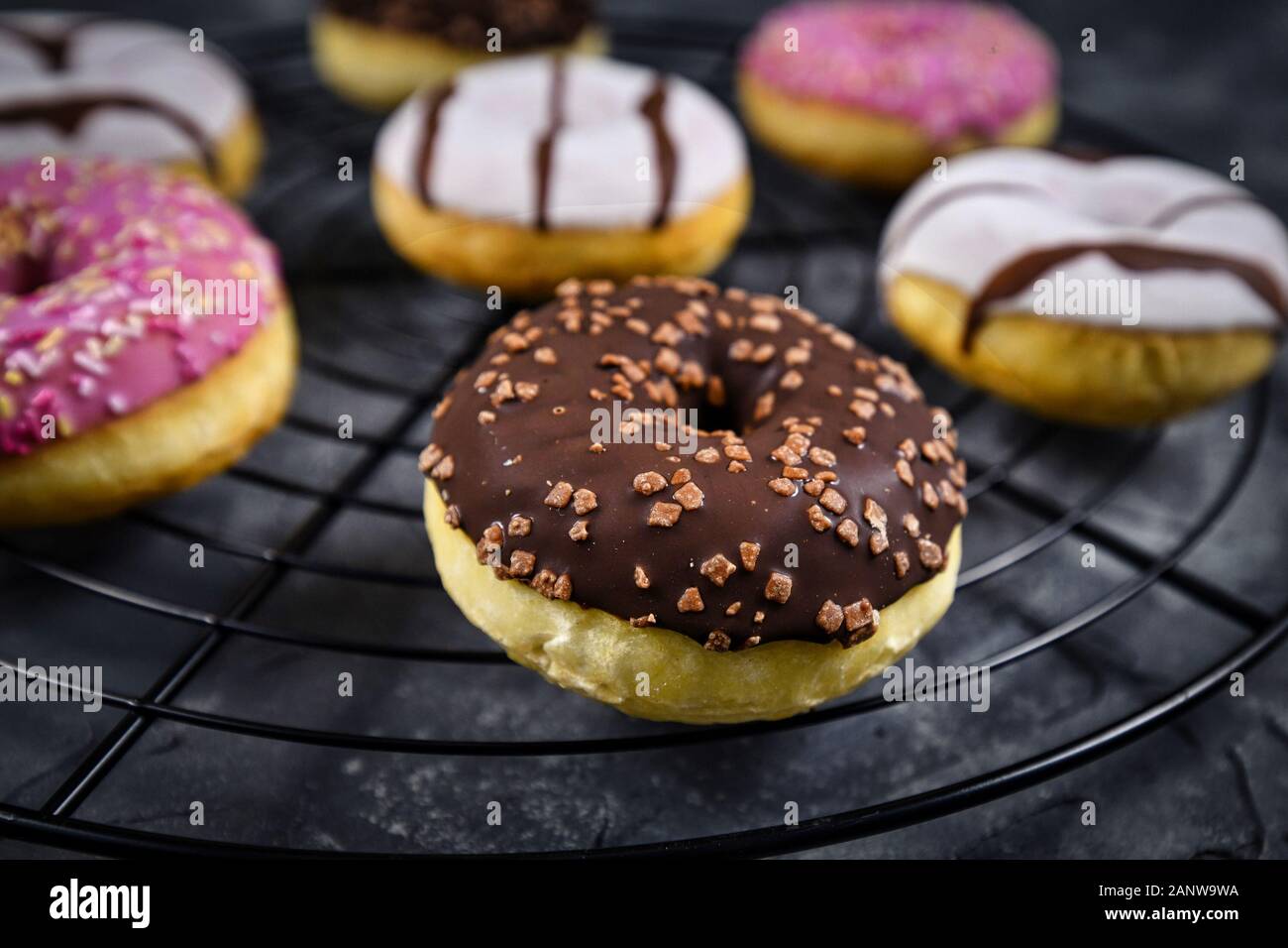 Tasty baked donut with brown chocolate glazing and sprinkles on cake grid  with other colorful donuts in background Stock Photo - Alamy