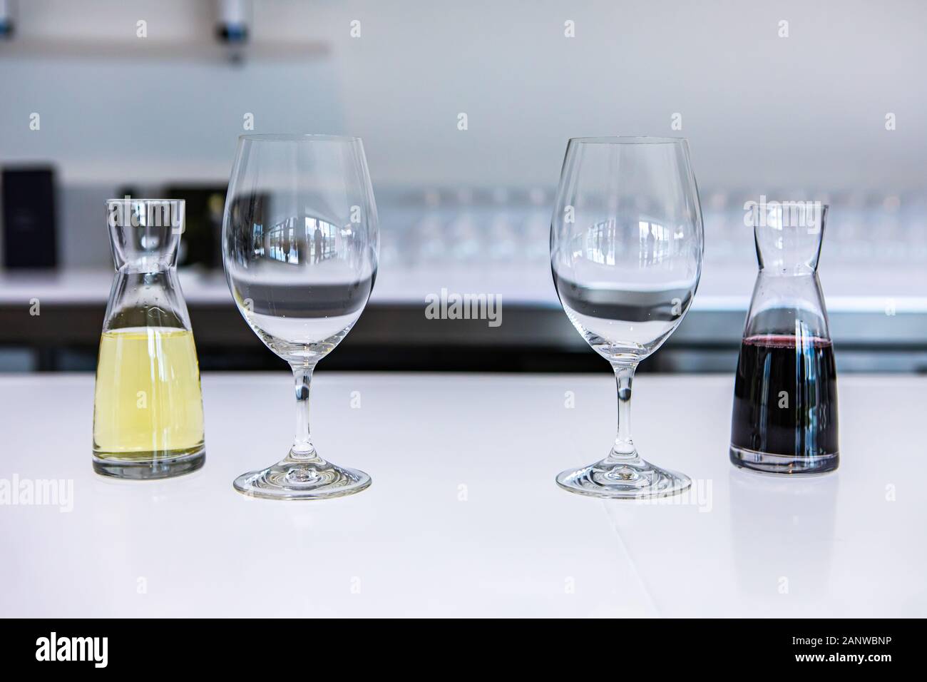 two empty wine glasses and a pair of small decanters filled with white and red wines, taste stemware on a bright white bar counter of the tasting room Stock Photo