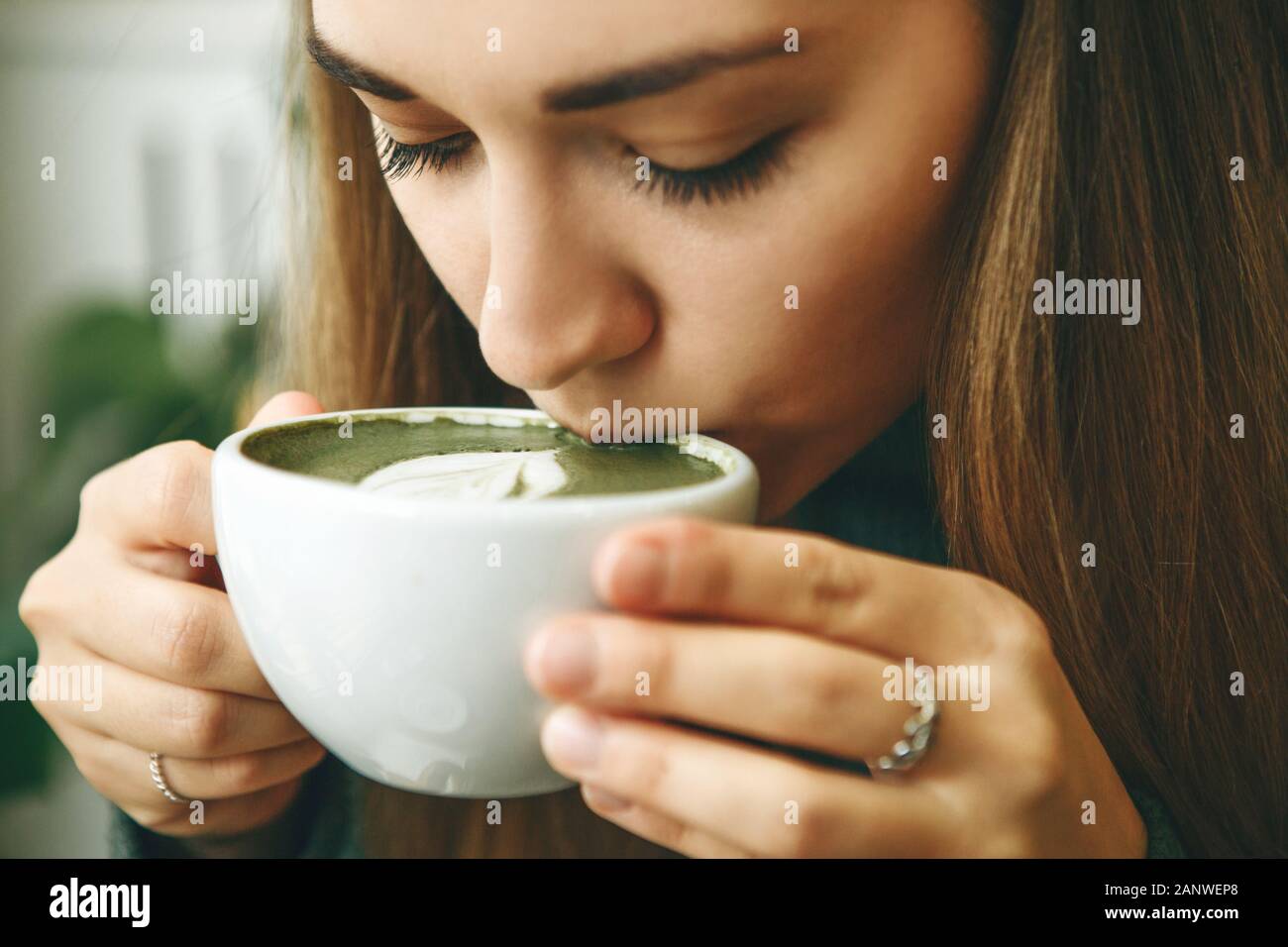 Close-up face or portrait of a girl who drinks healthy and delicious green matcha latte tea Stock Photo