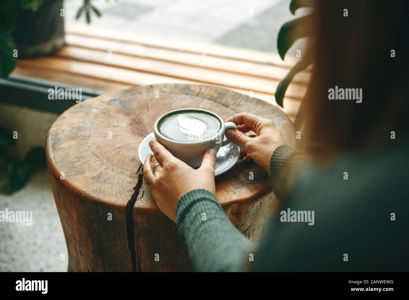 Girl drinks aromatic fresh and healthy green matcha latte tea in a cafe. Stock Photo