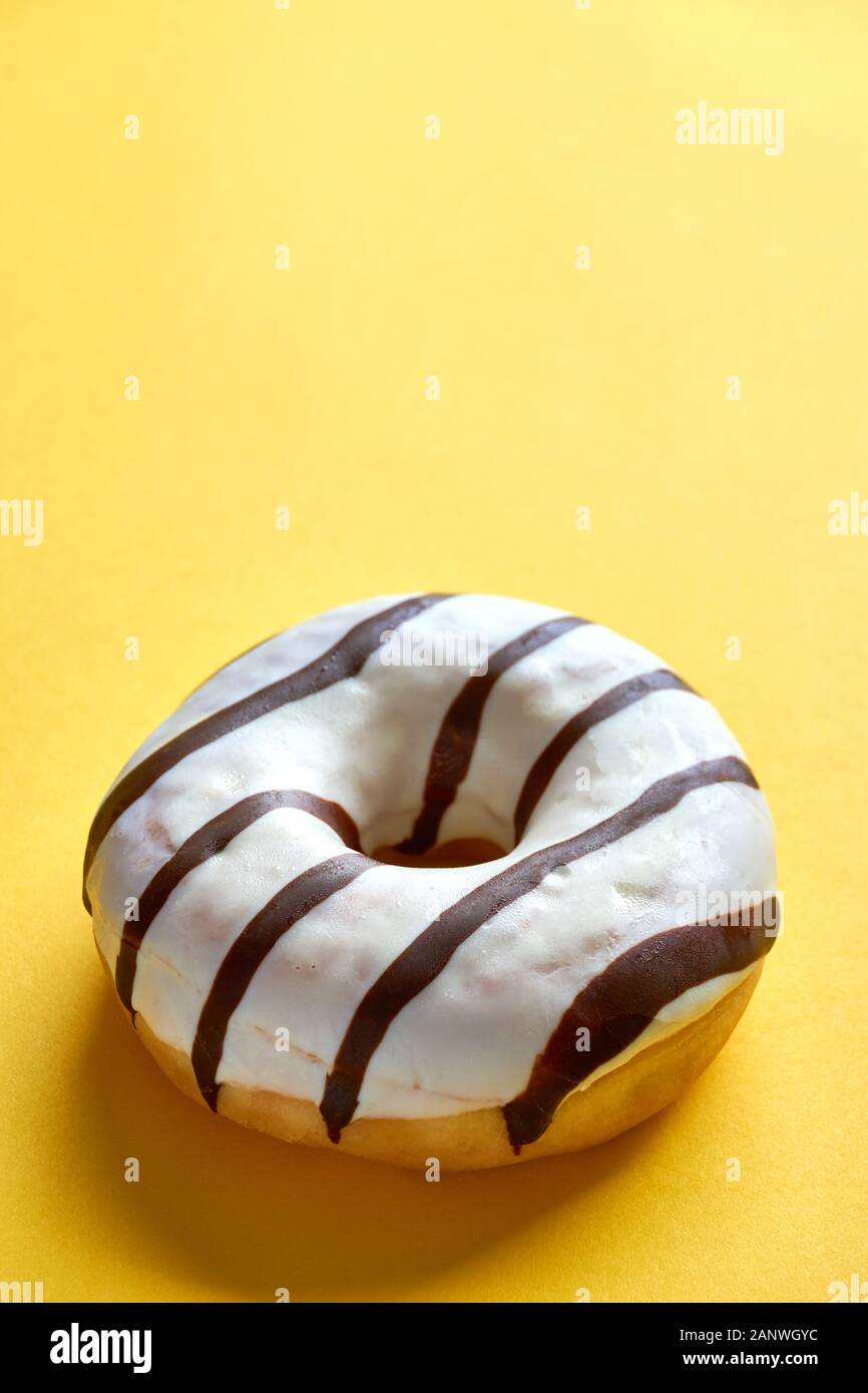 One single round donut with white ice glazing and stripes of dark brown chocolate on a yellow background with copy space. Vertical image Stock Photo
