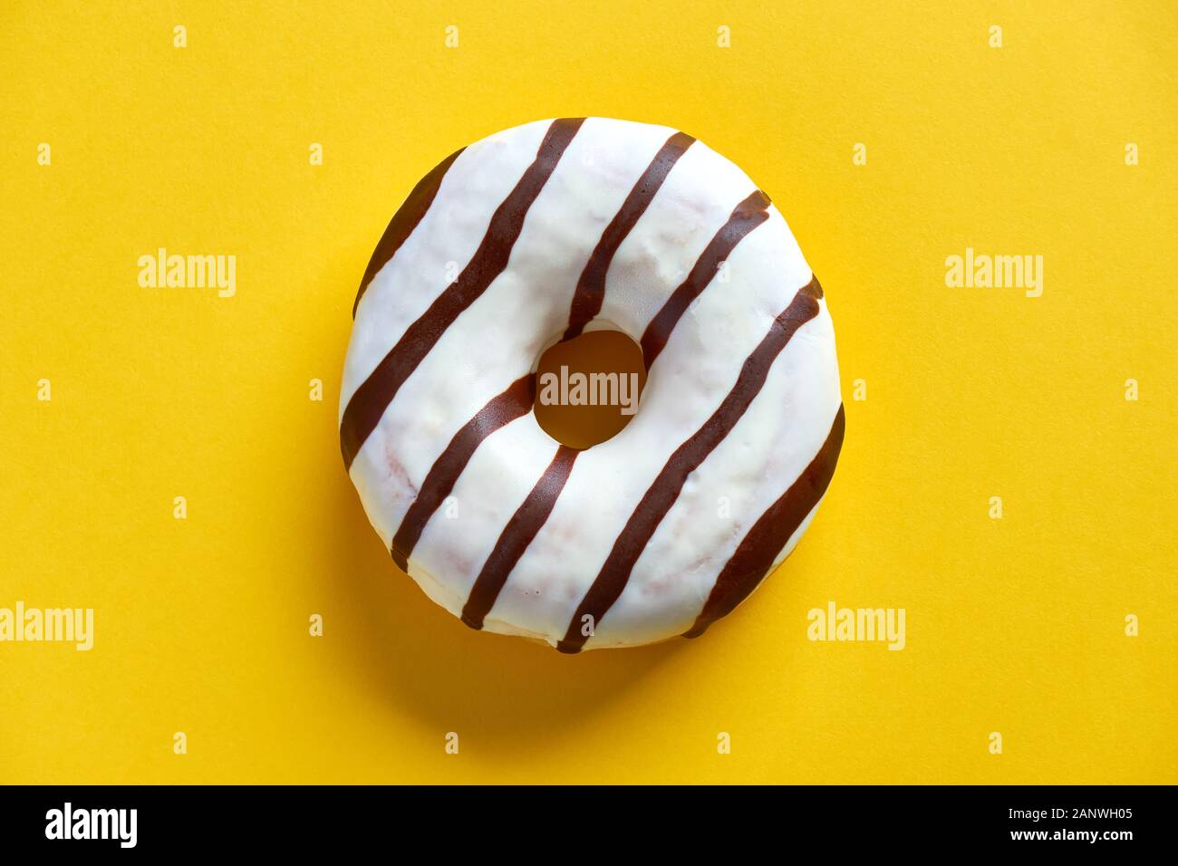 One single round donut with white ice glazing and stripes of dark brown chocolate on a yellow background with copy space. Flat lay. Stock Photo