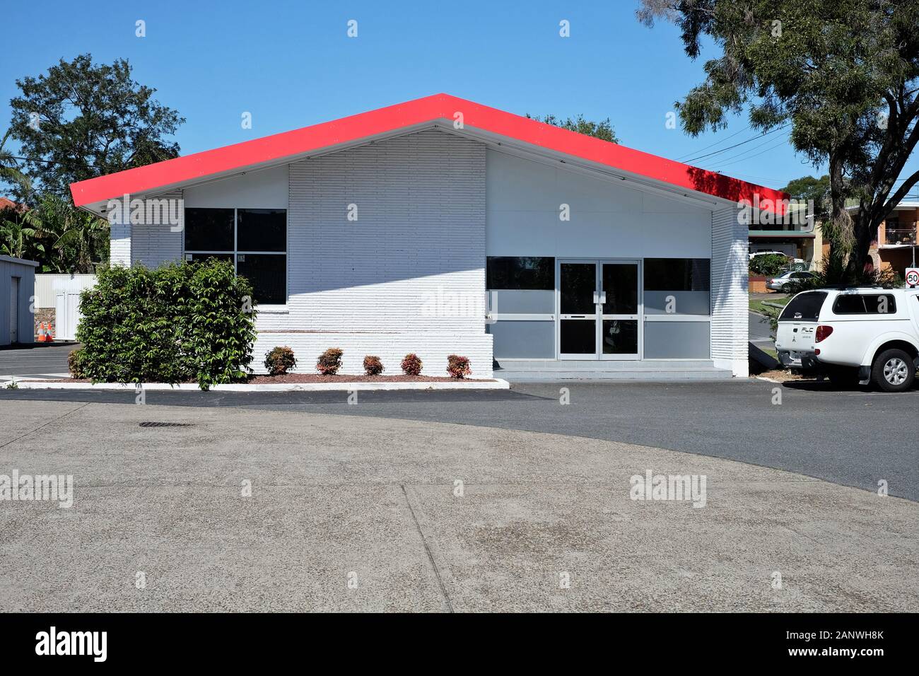 Commercial building roof ,double doors, white with red roofline barge boards, petrol station driveway  some green shrubs and blue sky Cannon Hill Stock Photo