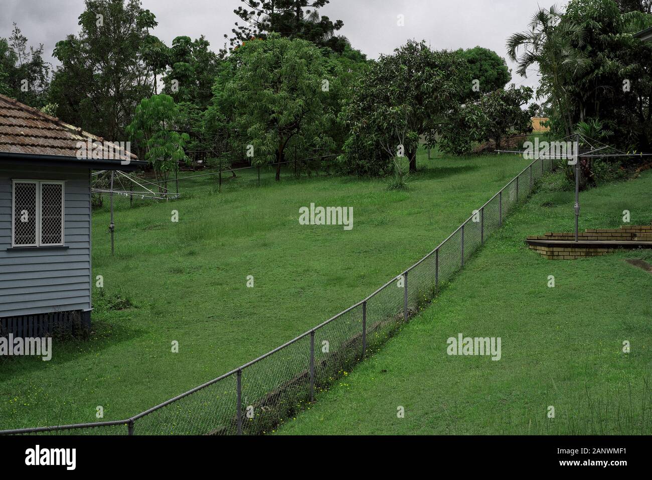 A long wire fence between two lush green grassy and very deep back yards of  Post War housing commission Houses in the Brisbane suburb Seven Hills Stock Photo