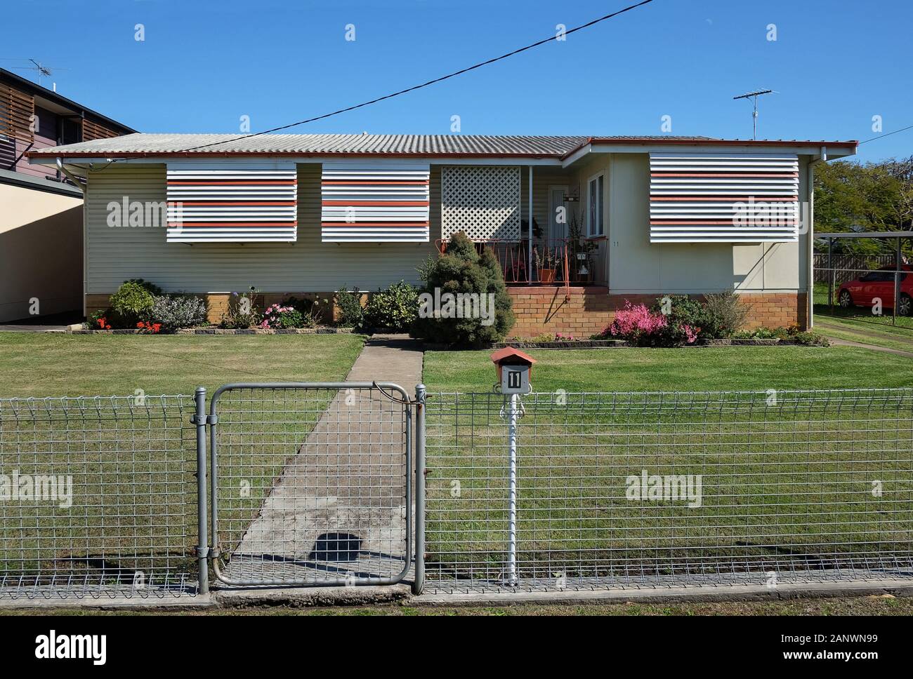 Low set 1960s mid century modern inspired house in Cannon Hill . Green lawn, wire fence, grass lawn, weatherboard, fibro & aluminium louvre awnings Stock Photo