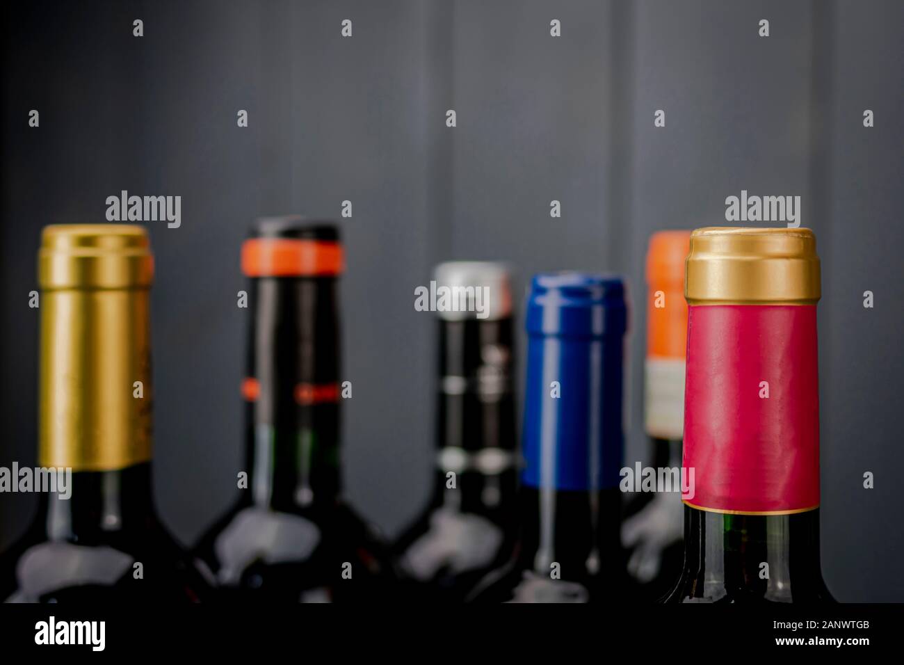 Set of unopened red wine bottle labels from different manufacturers with different color labels on gray wooden background Stock Photo