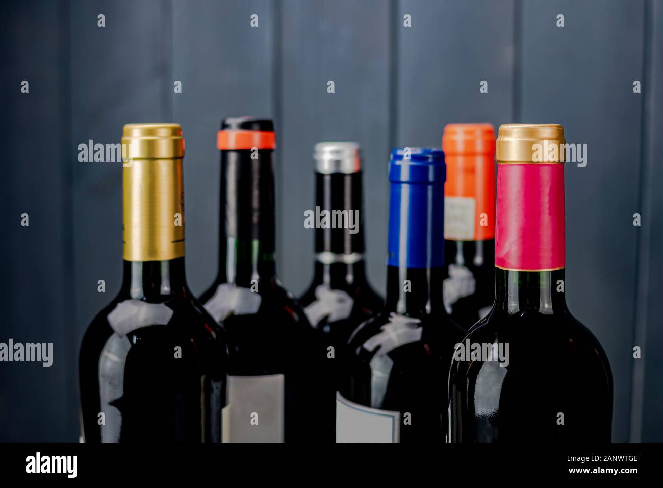 Set of labeled and unopened red wine bottles from different manufacturers with different color labels on gray wooden background Stock Photo