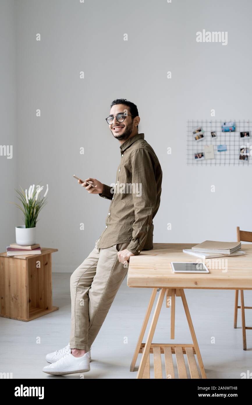 Young cheerful businessman using smartphone while standing by table Stock Photo