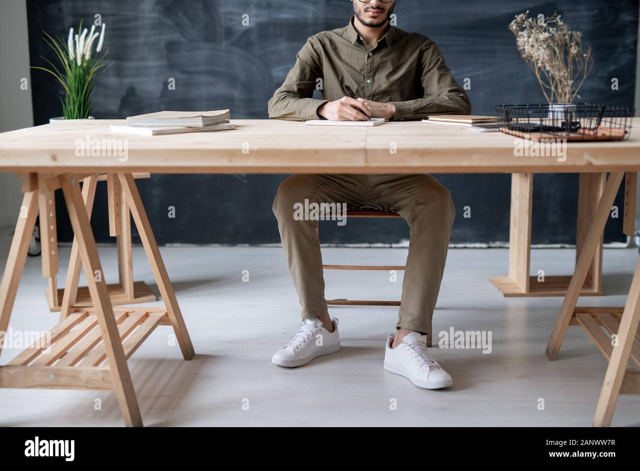 Young casual student sitting by wooden table while writing essay at lesson Stock Photo