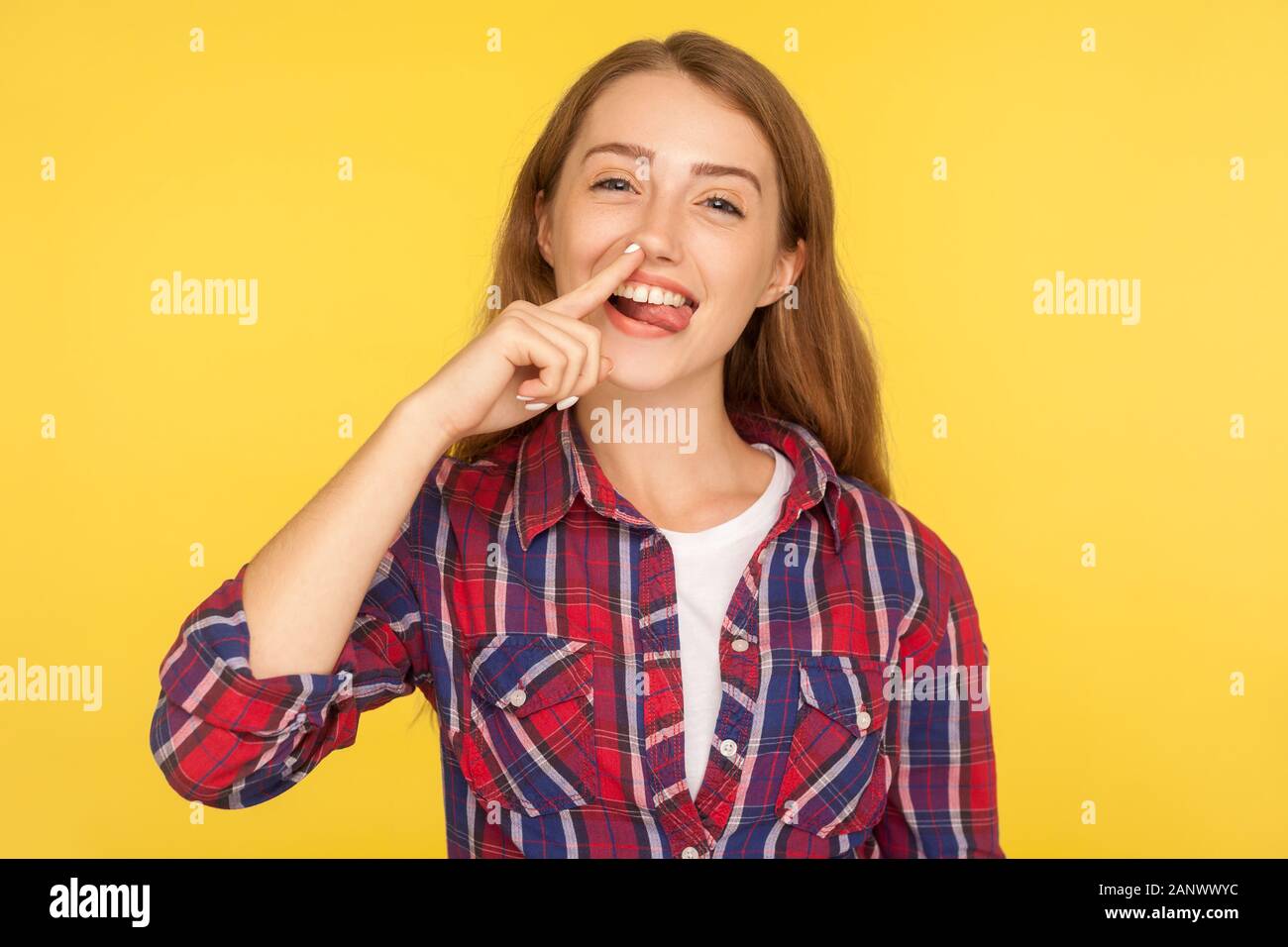 Portrait of funny childish ginger girl in checkered shirt picking her nose and demonstrating tongue with comical silly expression, pulling out boogers Stock Photo