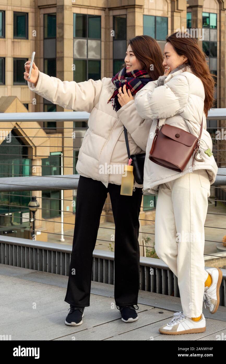 Millennium Bridge London people Two young Asian women smiling and posing for photo and taking selfie on the Millennium Bridge in London, UK Stock Photo