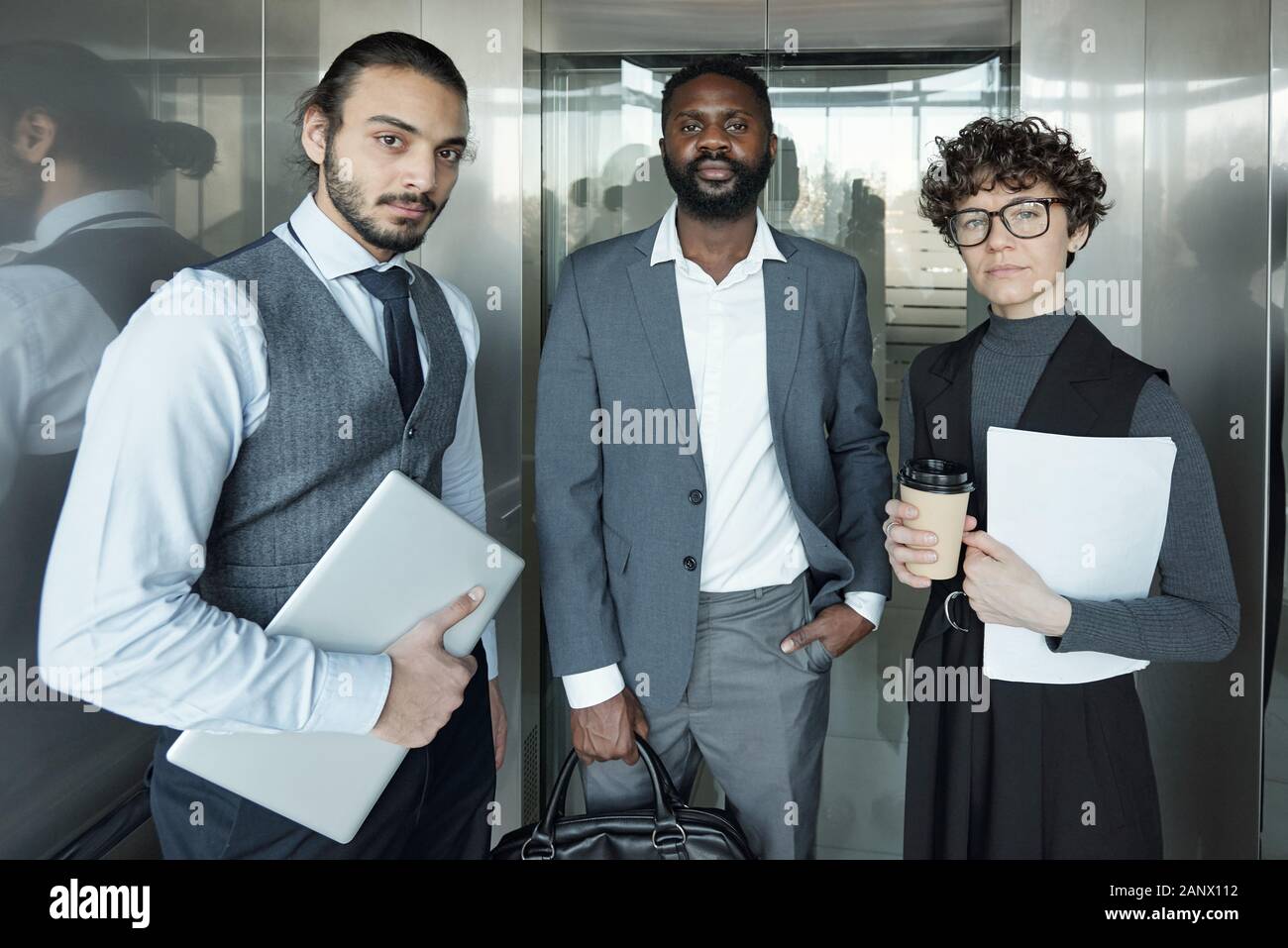 Young businesswoman and two intercultural businessmen moving in elevator Stock Photo