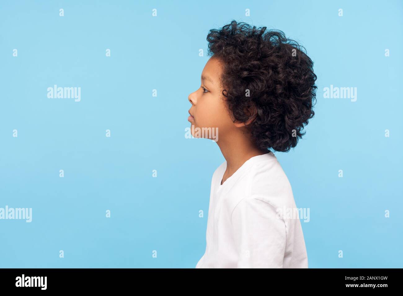 Profile of pretty nice little boy with stylish curly hair in T-shirt looking to side with serious attentive face, calm pensive expression. indoor stud Stock Photo
