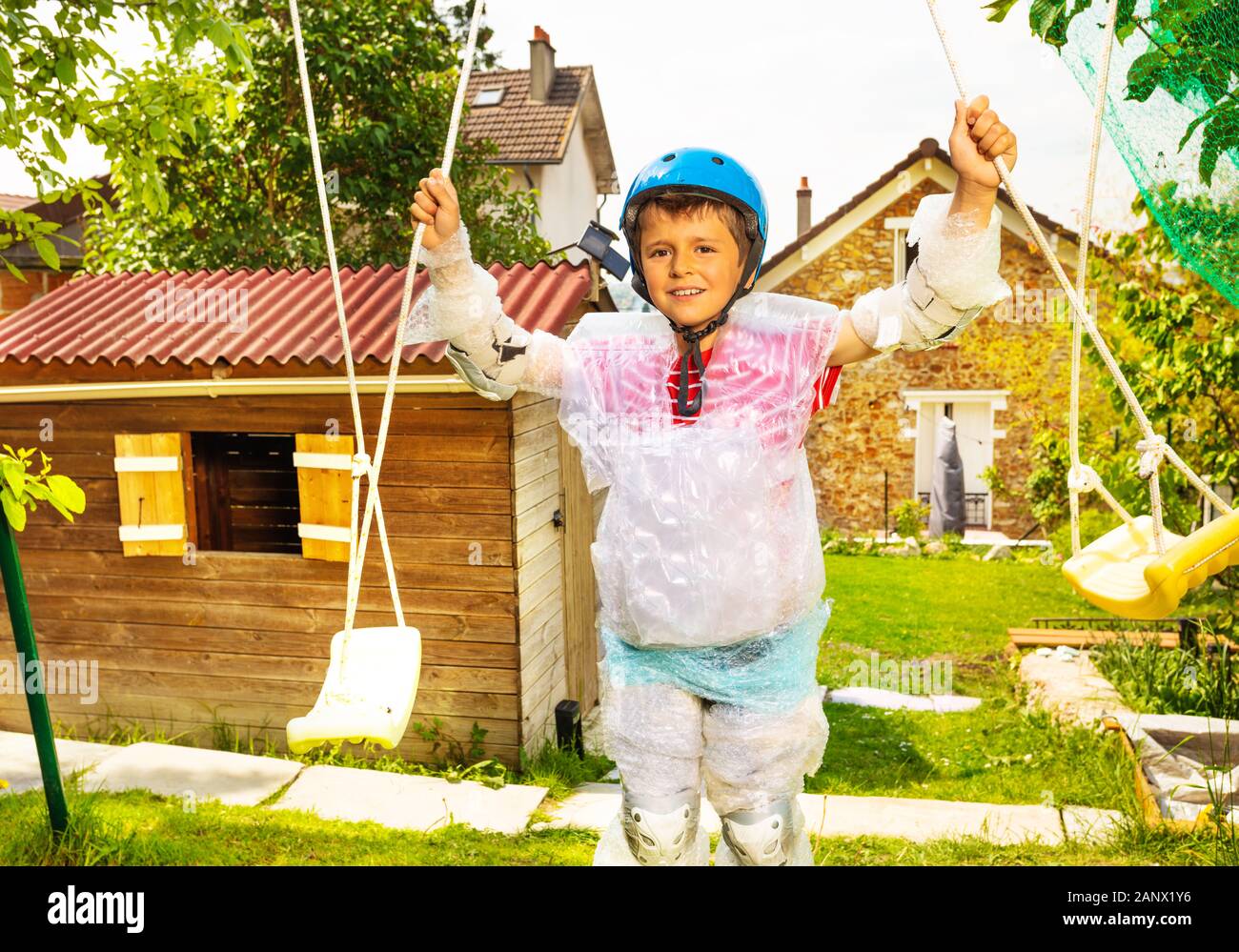 Super safe child in bubble wrap and helmet stand near swings in the