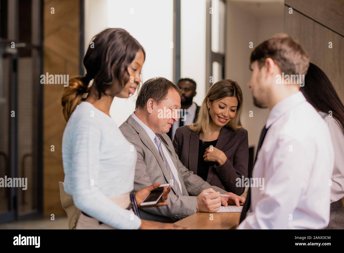 Group of contemporary businesspeople communicating by reception counter in hotel Stock Photo