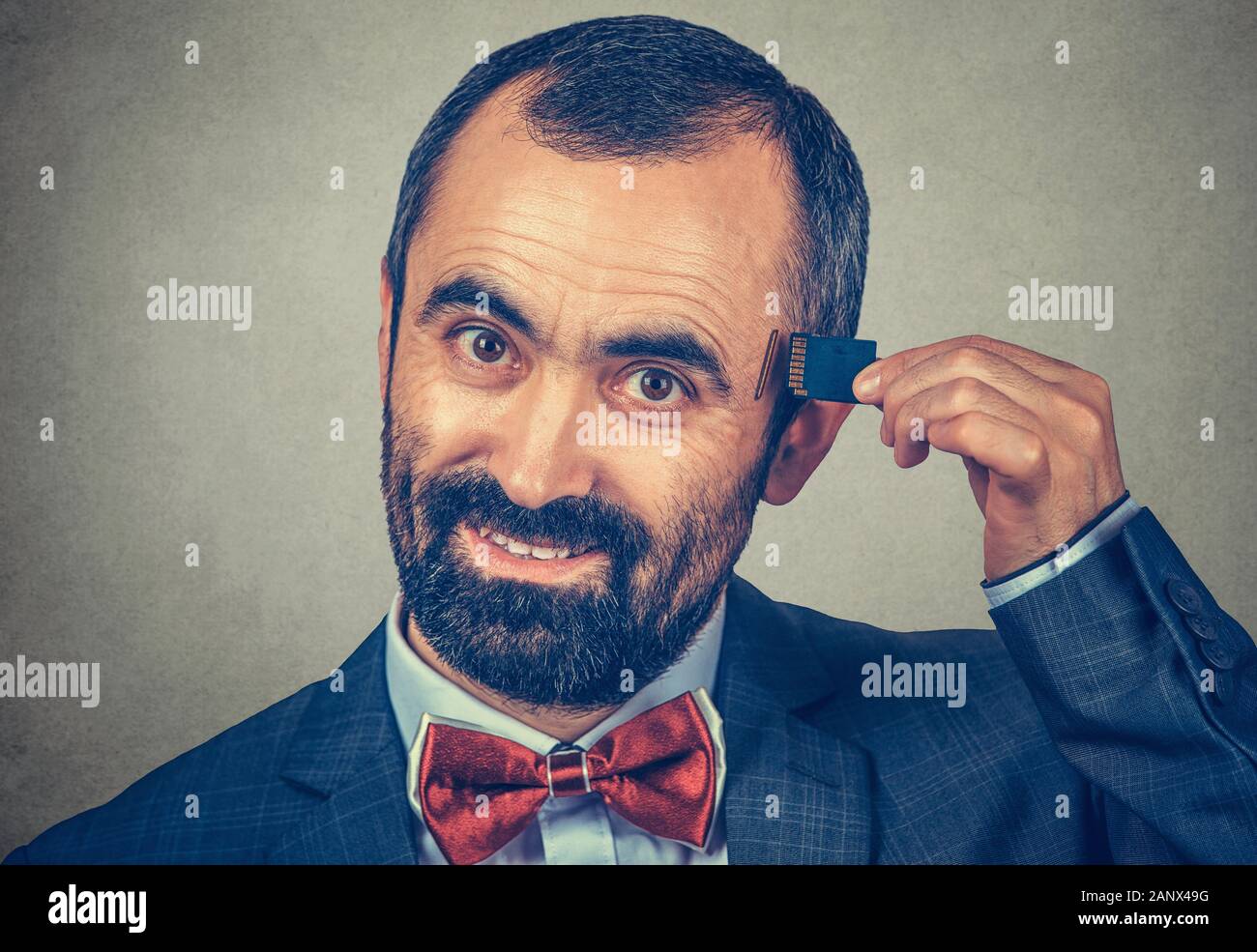 External memory needed concept. Portrait of a smiling bearded businessman wearing elegant jacket and red bow tie holding Micro SD card near his head i Stock Photo