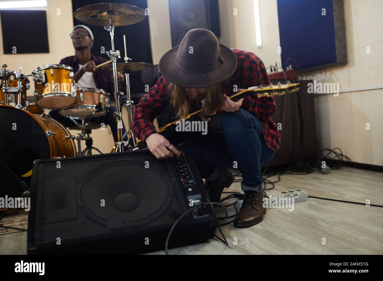 Full length portrait of contemporary musician setting up guitar amplifier during sound check while preparing for concert or rehearsal with band in background, copy space Stock Photo