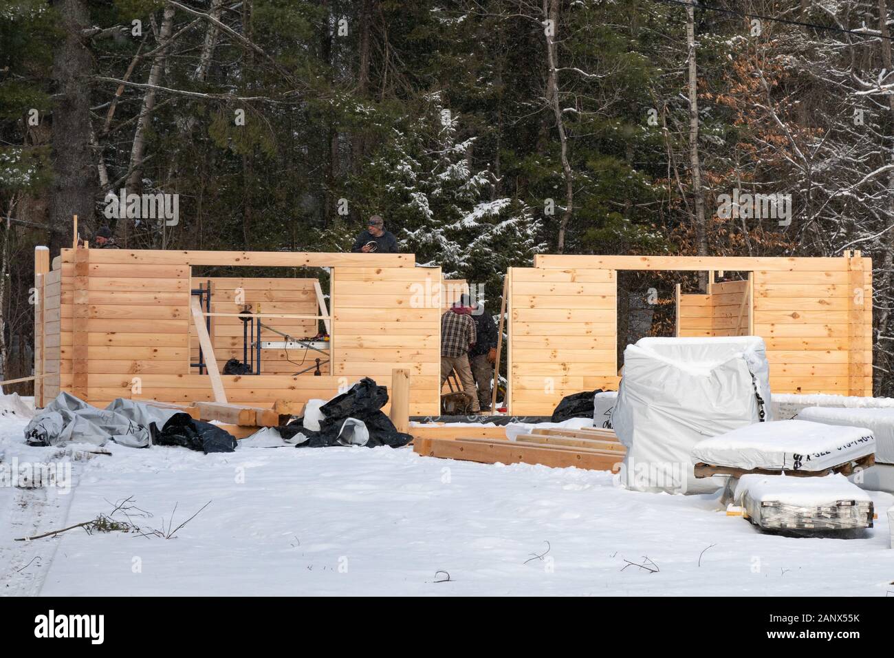 Three construction workers assembling a manufactured log home on a cold winter day in the snow in Speculator, NY USA Stock Photo