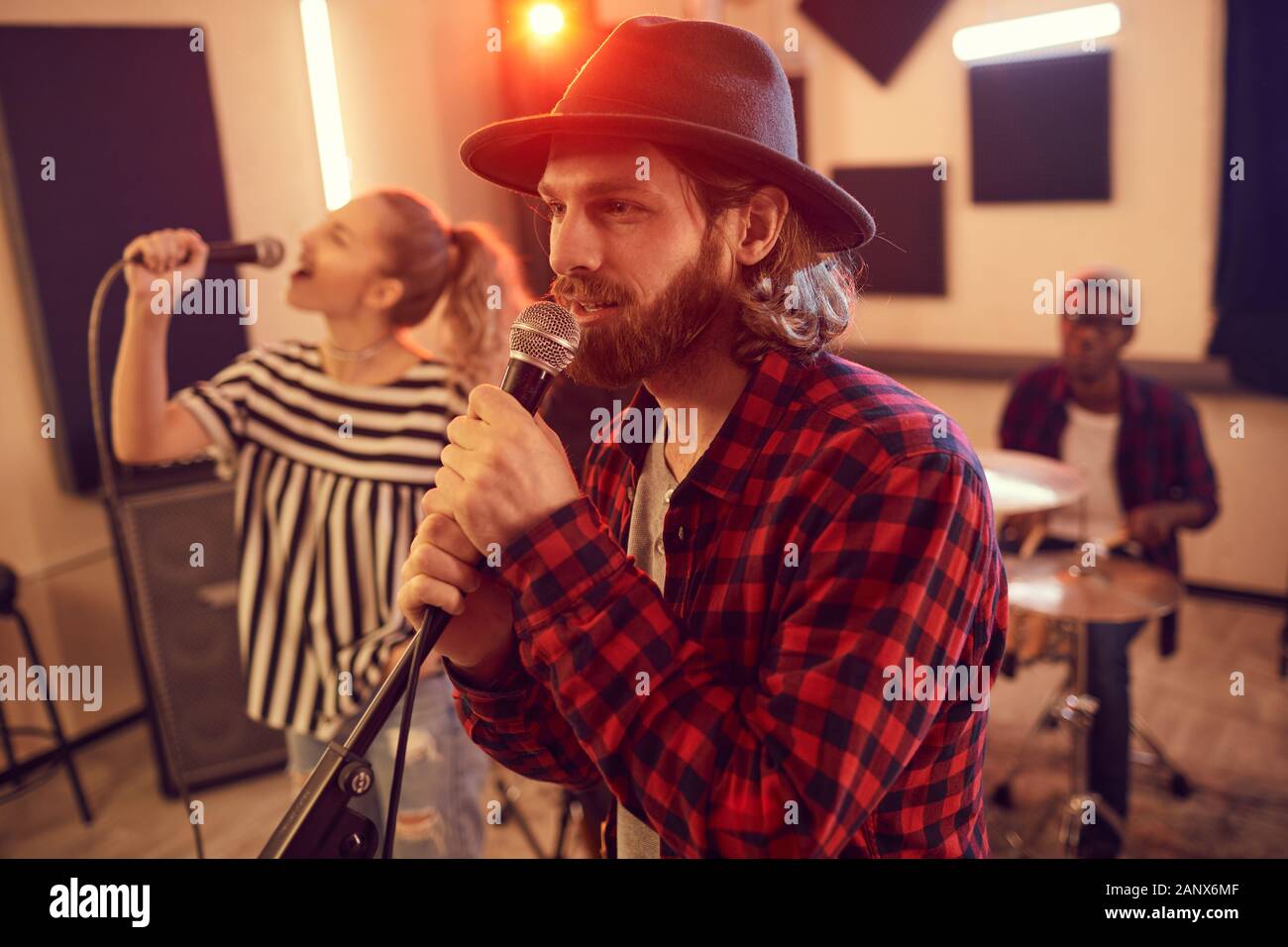 Side view portrait of handsome bearded man singing to microphone during rehearsal or concert with music band, copy space Stock Photo