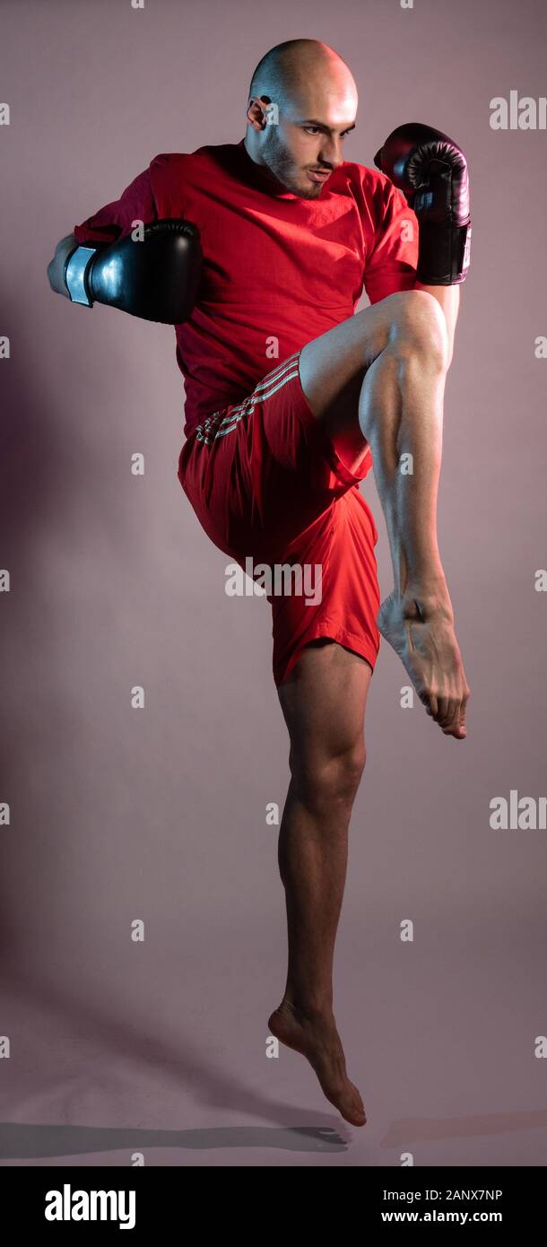 Boxer lifts leg moving away from hitting him in black gloves and red shorts Stock Photo